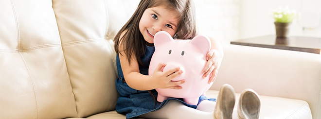 Young smiling girl with long, brown hair sitting on couch hugging large pink piggy bank